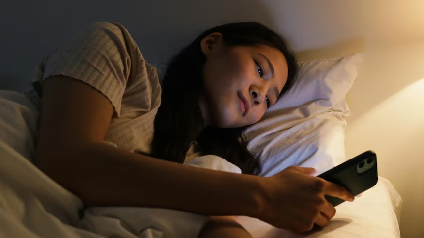 Teen lying in bed late at night looking at a phone